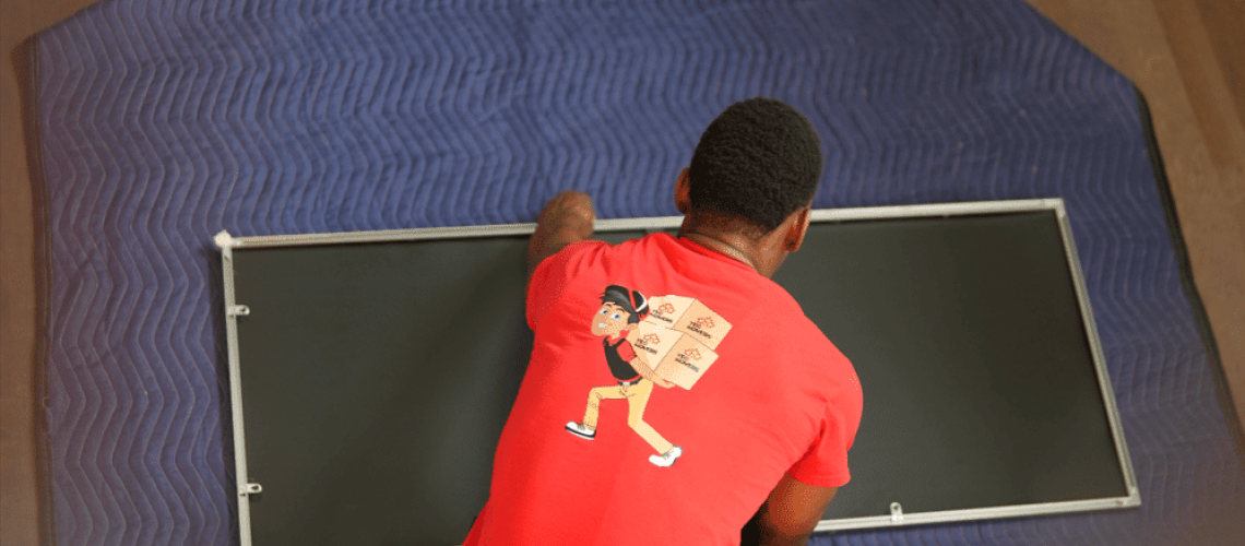 Man packing a mirror carefully on a moving blanket for safe transport.