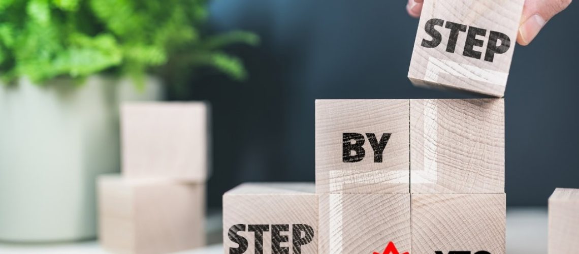 Hand stacking wooden blocks with "STEP BY STEP" for moving process.