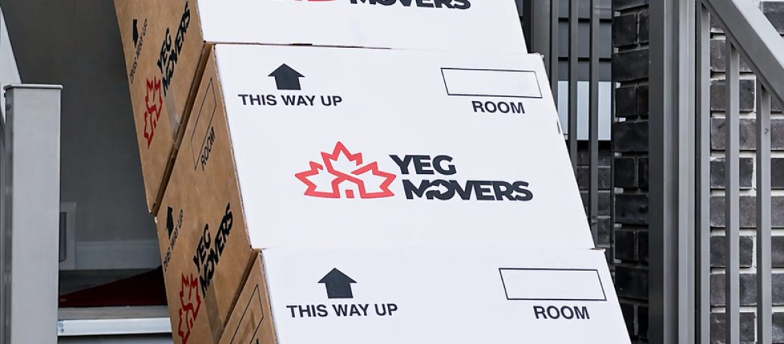 yeg movers professional transporting stacked boxes down stairs using a dolly, showcasing safe handling and efficient residential moving services in edmonton