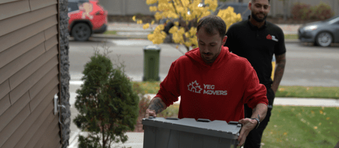 Professional movers carrying a box outside a residential building in Edmonton.