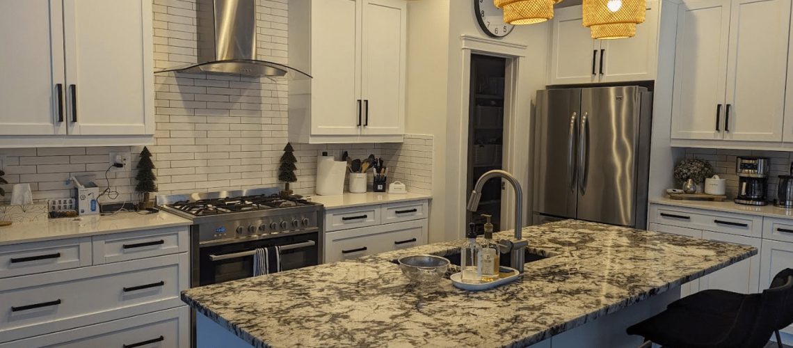 Modern kitchen with white cabinets, stainless steel appliances, pendant lights, and a large marble island.