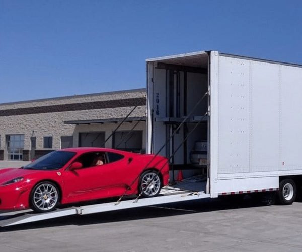 Red sports car being loaded into an enclosed auto transport trailer.
