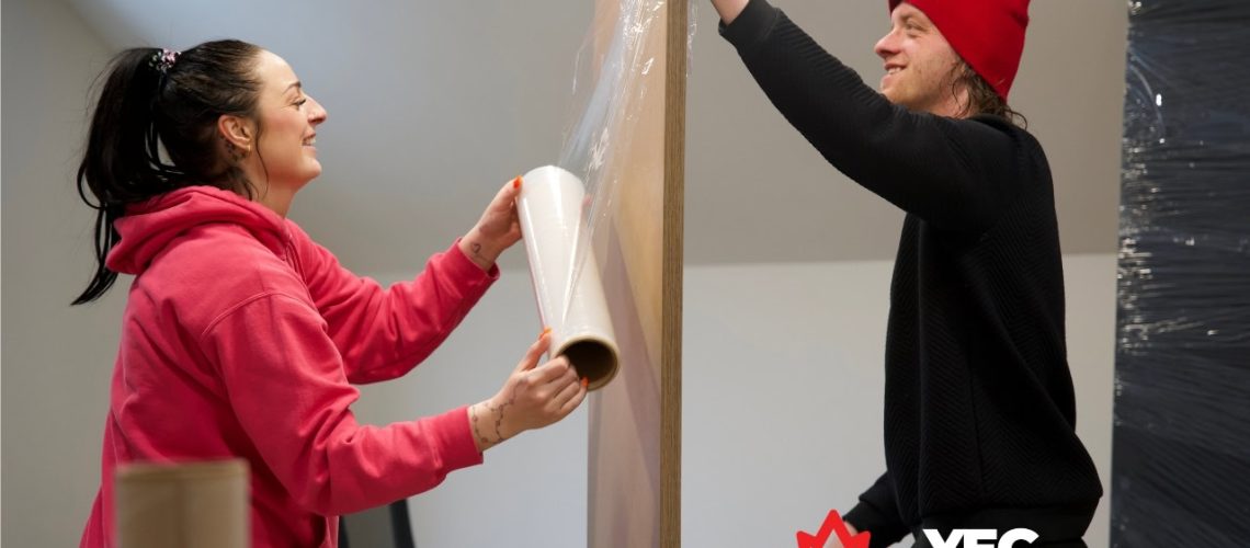 Two movers packing a large wooden panel with plastic wrap in Edmonton.
