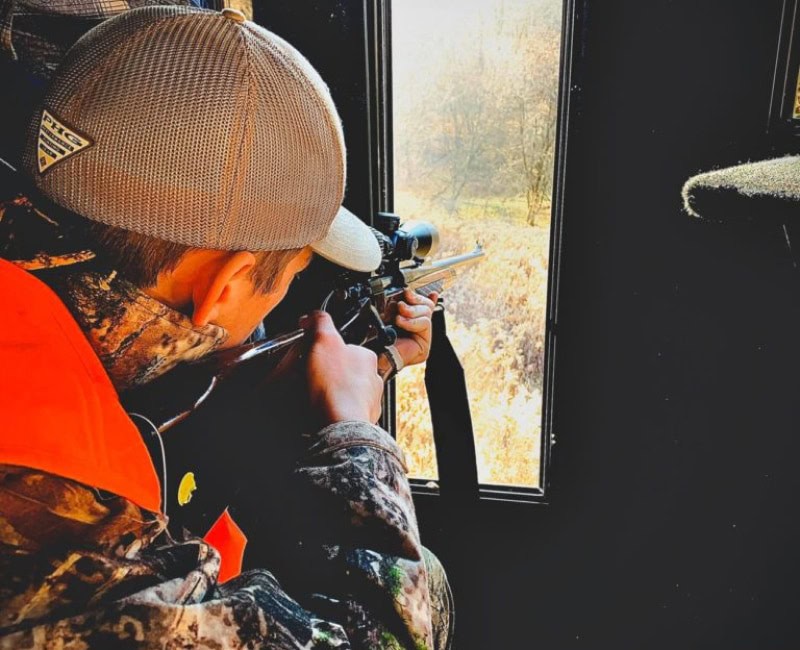 hunter pointing rifle out of blind window