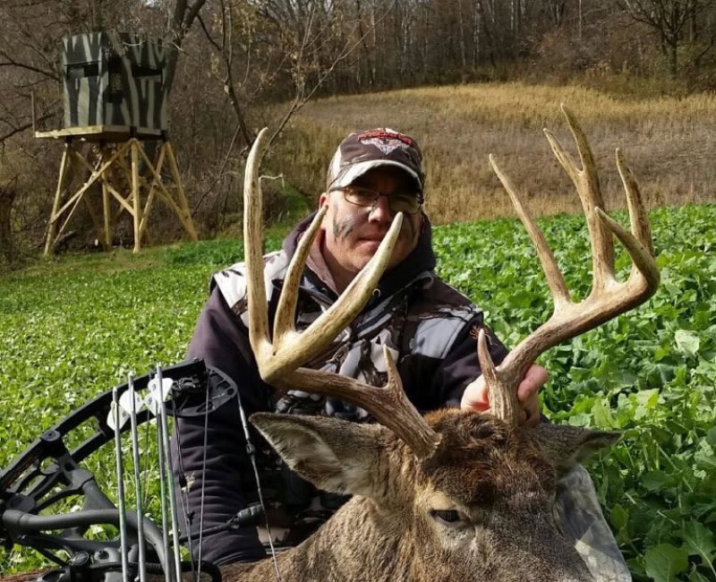 hunter posing with deer and hunting blind in the background