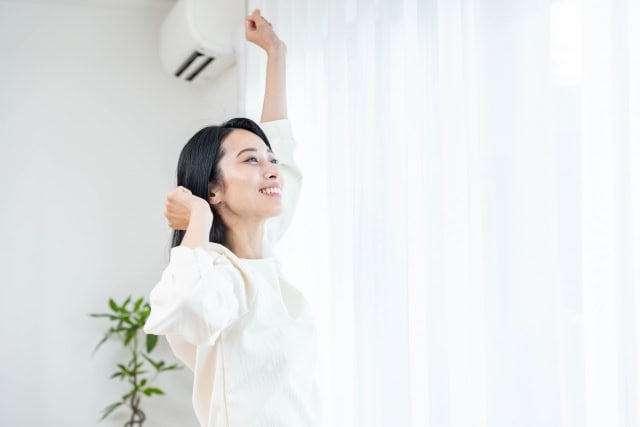 朝の光の中で気持ちよくストレッチをする40代女性