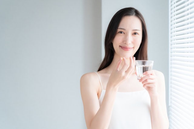 サプリメントを手に取り、水と一緒に飲もうとする40代女性