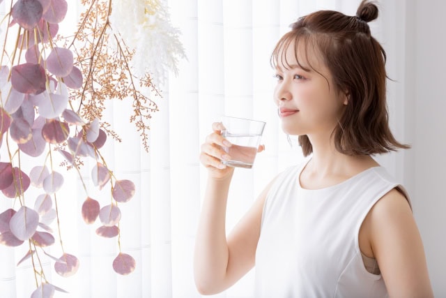 窓辺で水を飲む女性とプラセンタサプリのカプセル入りバナー