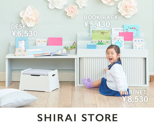 「子どもの片づけ習慣を育てるキッズ収納シリーズ。白いデスク・本棚・キャビネットと女の子が楽しそうに座っている様子」