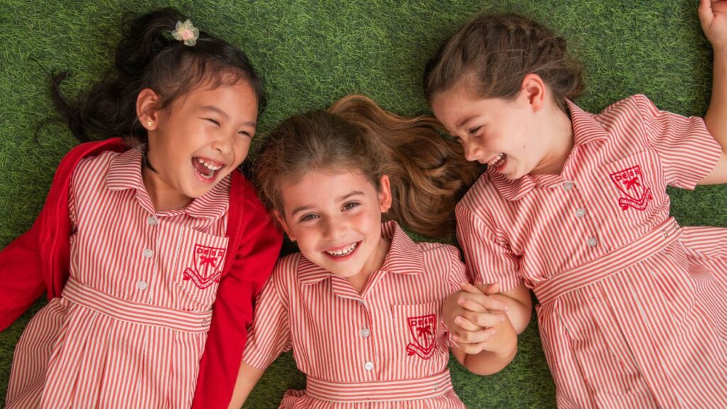 Happy schoolgirls in red and white uniforms lying on grass.