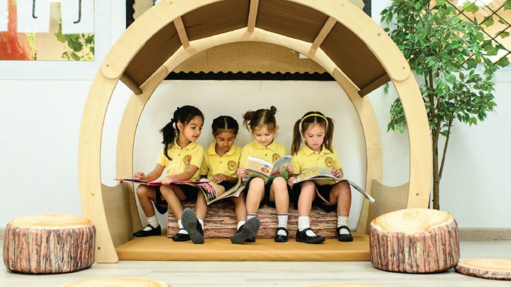 Four young girls reading books together in a cozy indoor reading nook.