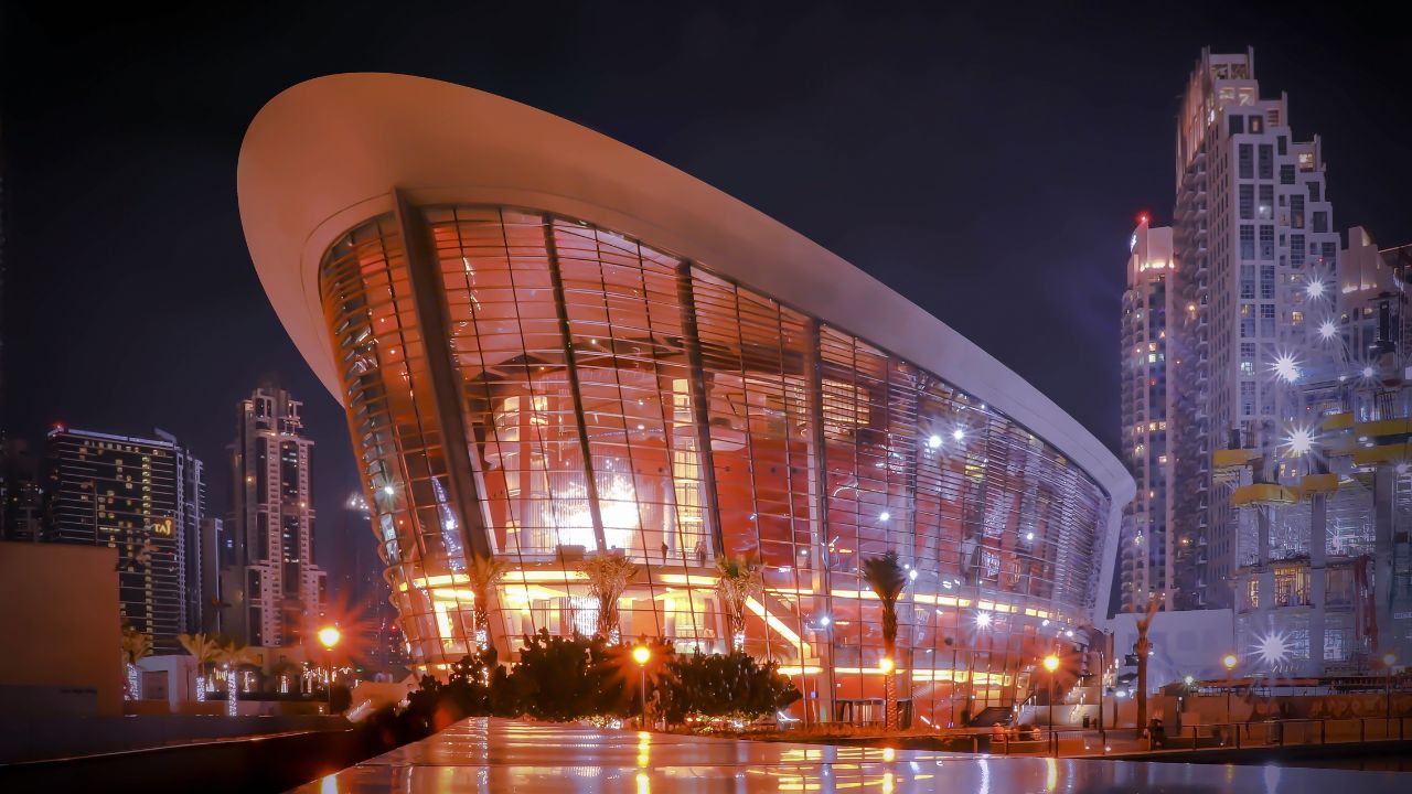 Dubai Opera illuminated at night with modern architecture and city skyline.