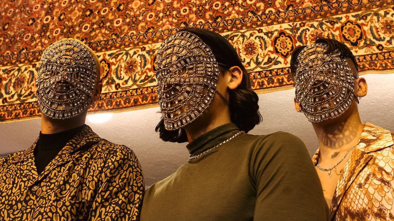 Three performers with ornate, beaded masks at Glass Beams event in Dubai.