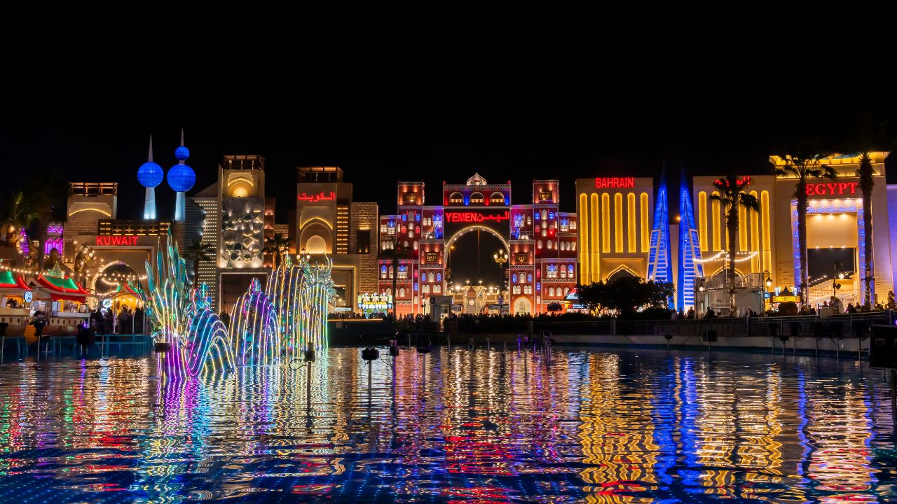 Vibrant night view of Dubai's Global Village with colourful lights and reflections on water.