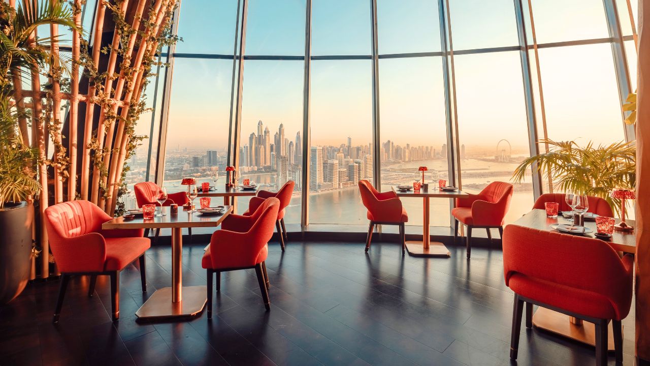 View of Dubai skyline from a stylish restaurant with red chairs and panoramic windows.