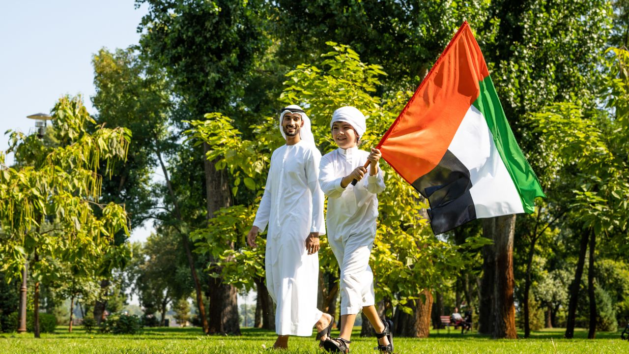 UAE National Day celebration with people holding the national flag in a park.