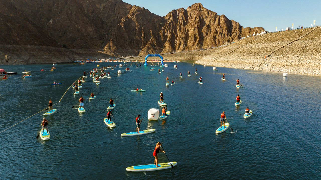 People paddleboarding at Dubai's reservoir with mountains in the background.