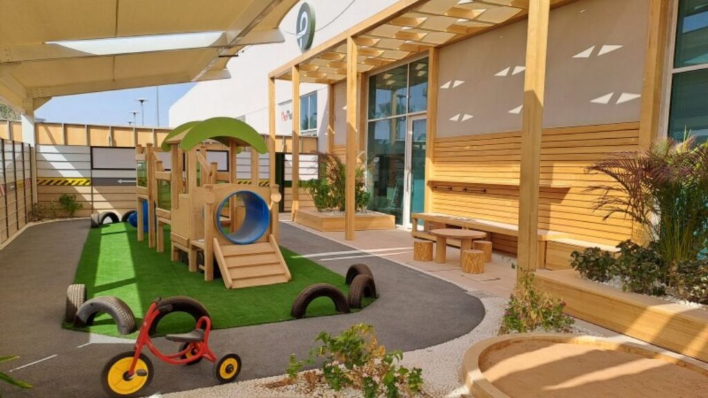 Outdoor play area at Redwood Montessori Nursery with slides, tricycles, and soft turf.