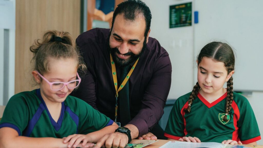 Teacher with two young students in classroom, engaging in learning activity.