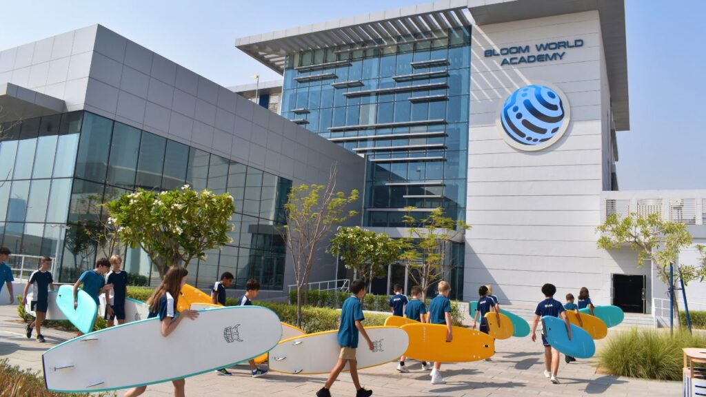 Modern Bloom World Academy building with students and surfboards outside.