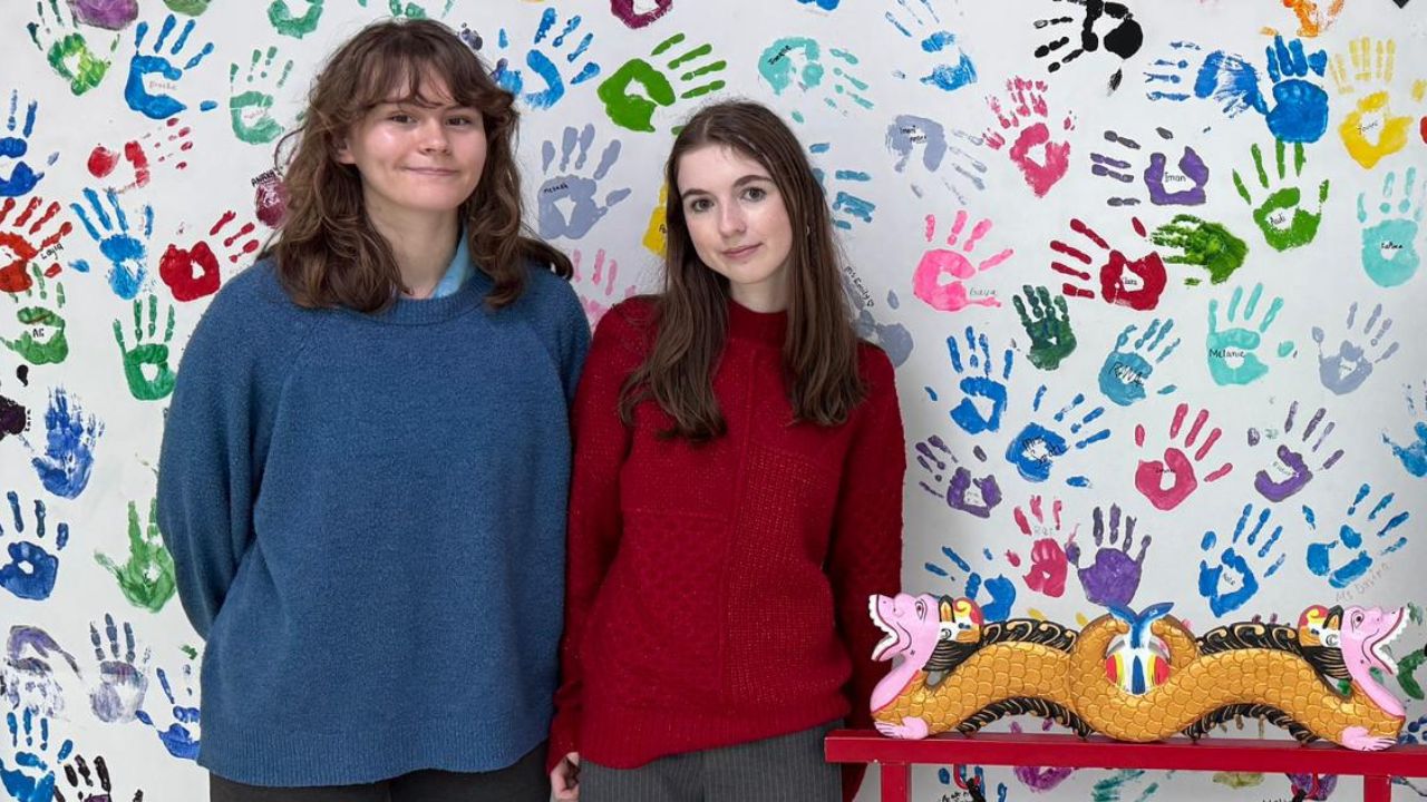 Two students standing in front of a colourful handprint wall at Yalla Dubai Life.
