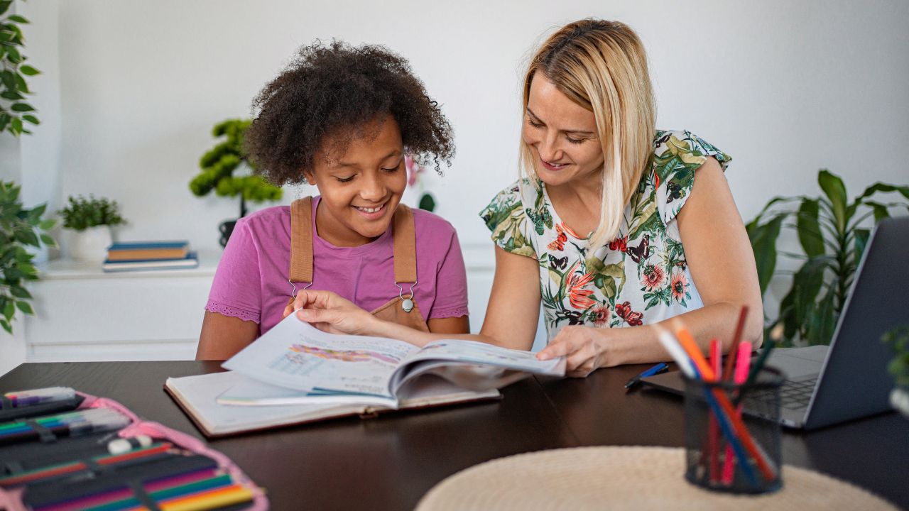 Tutor assisting a young girl with her homework in a well-lit, modern classroom setting.