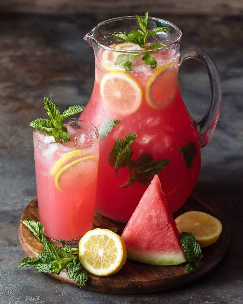 A refreshing glass of homemade watermelon lemonade, garnished with fresh mint and lemon slices, served over ice on a sunny summer day.