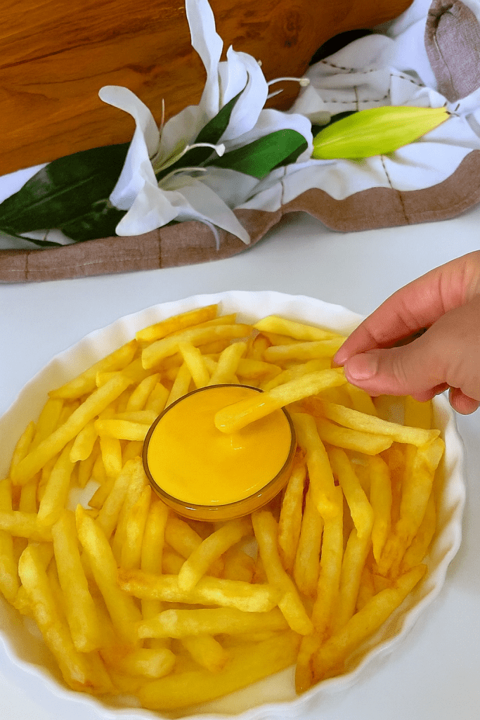 French fries served on a white plate with a bright yellow cheese sauce in the center, featuring crispy golden potato sticks arranged neatly around the bowl.