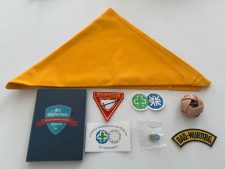Verschiedene Pfadfinder-Accessoires, darunter ein gelber Halstuch, Abzeichen, Mitgliederbuch, Buttons und eine Ballknoten, auf weißem Hintergrund, ideal für Pfadfinder- und Jugendarbeit.