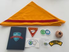 Alt Text: Scout-Ausrüstung mit gelbem Halstuch, Abzeichen, Mitgliedsbuch, Knopf, Ball, Patch und Bändchen für Pfadfinder in Rheinland-Pfalz.