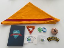 Farbenfrohes Pfadfinder-Set mit gelbem Halstuch, Abzeichen, Mitgliedsbuch, Kugel und Buttons für Kinder und Jugendliche, ideal für Pfadfindergruppen und Aktivitäten im Zentrallager.