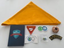 Pfadfinder Abzeichen und Zubehör auf weißem Hintergrund, inklusive gelbem Halstuch, Mitgliedsbuch, Abzeichen und Wurfknoten, ideal für Pfadfinderzentral Lager.