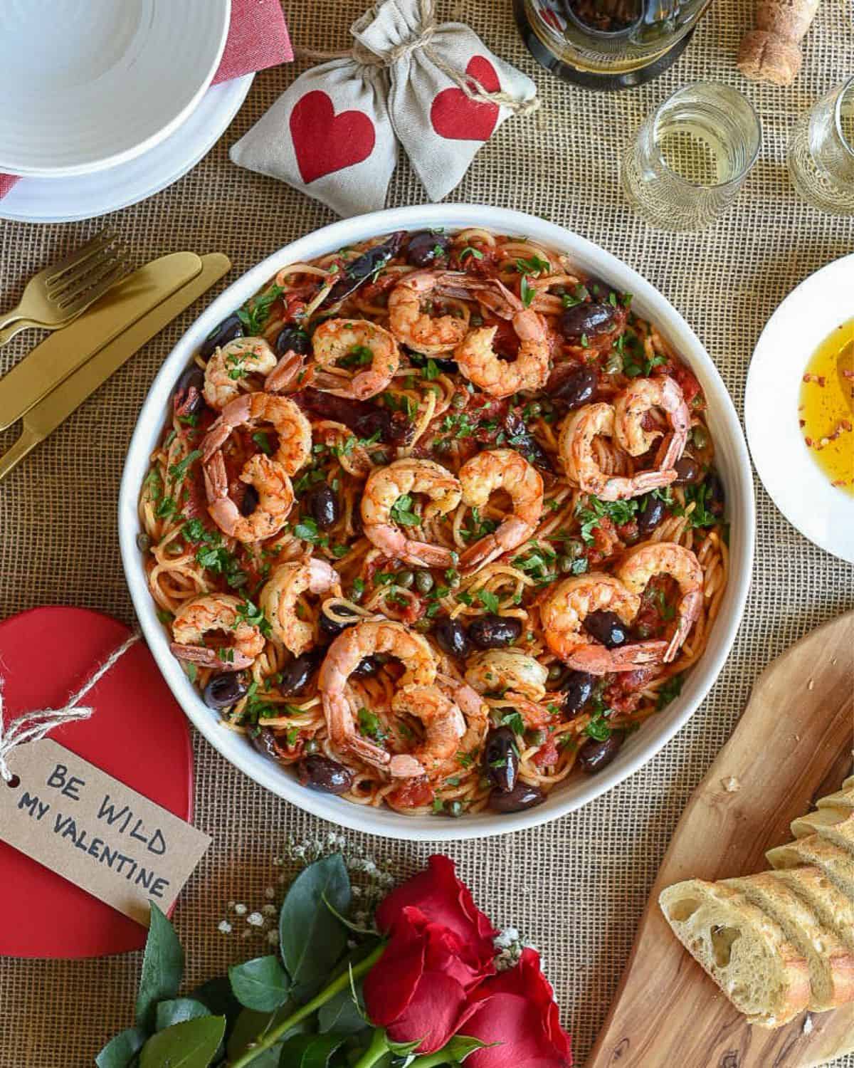 A top down image of a bowl of Pasta Puttanesca with Shrimp on a Valentine themed place setting.