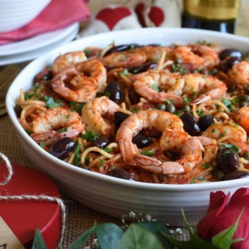 A large bowl of pasta with puttanesca sauce and shrimps placed like hearts.