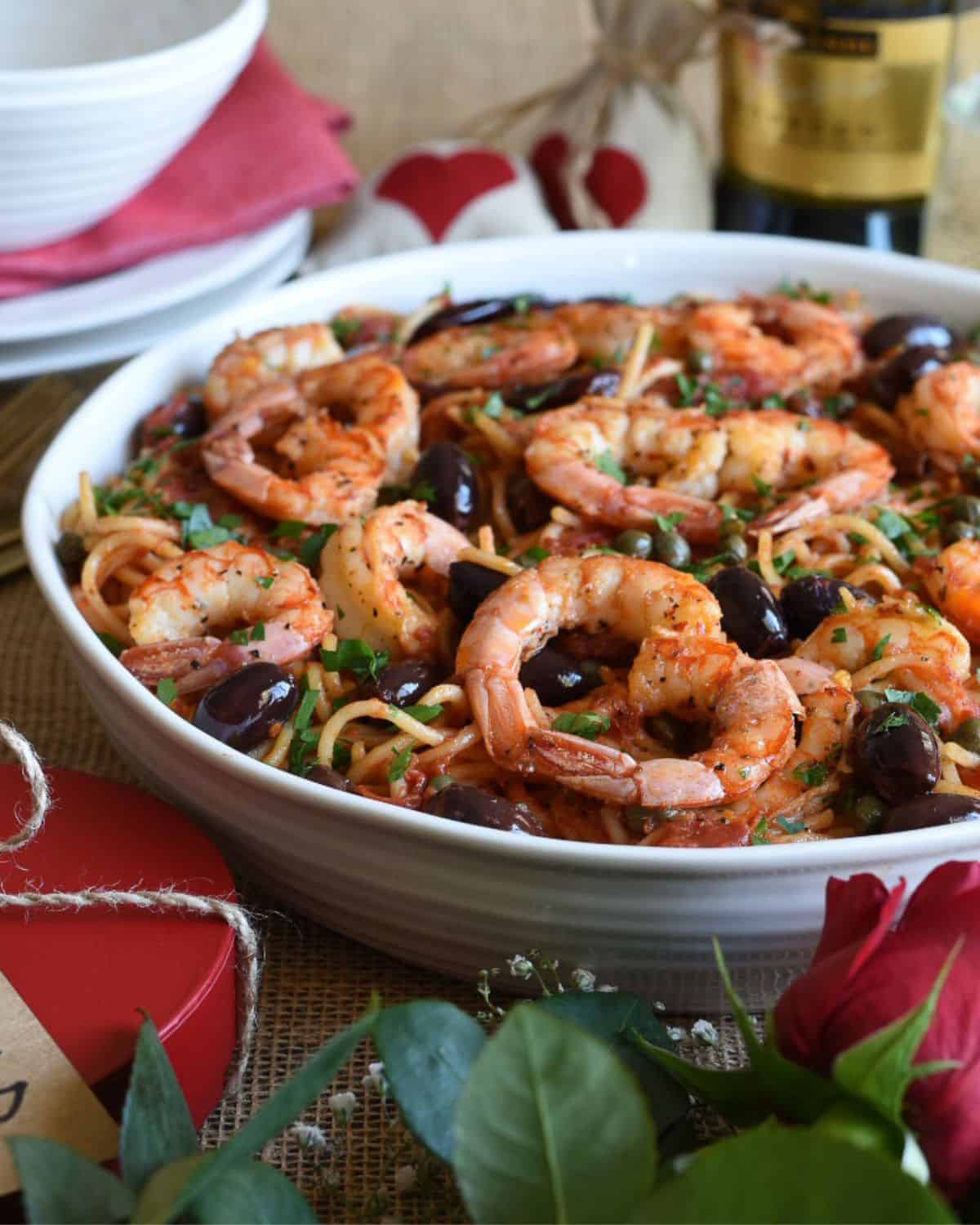 A large bowl of pasta with puttanesca sauce and shrimps placed like hearts.