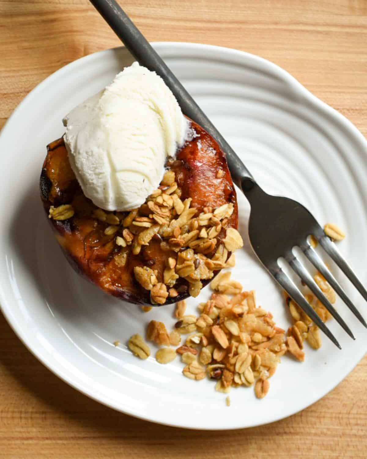 A grilled peach with a crumble topping and a scoop of vanilla ice cream.