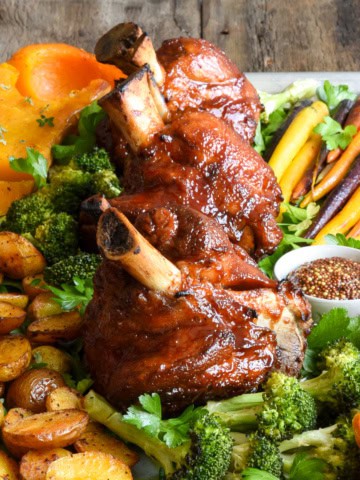 Three sticky BBQ pork hocks served with a variety of roasted veggies.