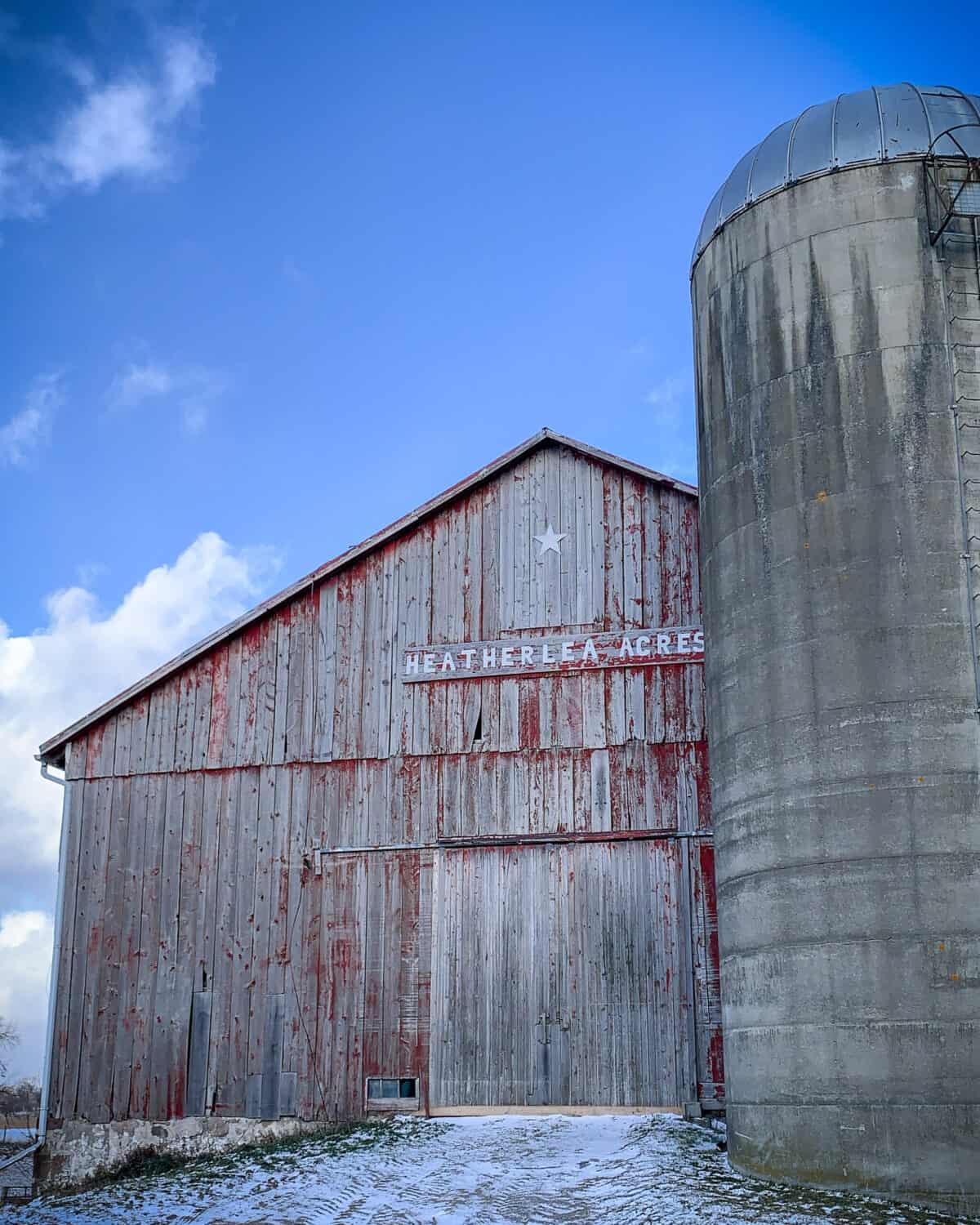 A faded red bar and silo on a snowy day with a blue sky.