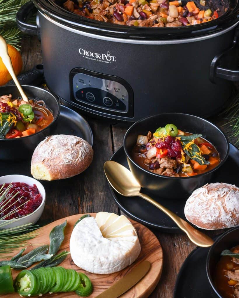 Image of a table with a crock-pot of turkey chili plus two bowls full of chili with bread. The table is decorated with Christmas evergreens and ornaments.