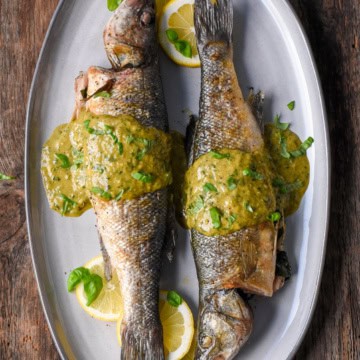 Two grilled branzinos on a plate with lemon slices and jalapeño-basil vinaigrette.