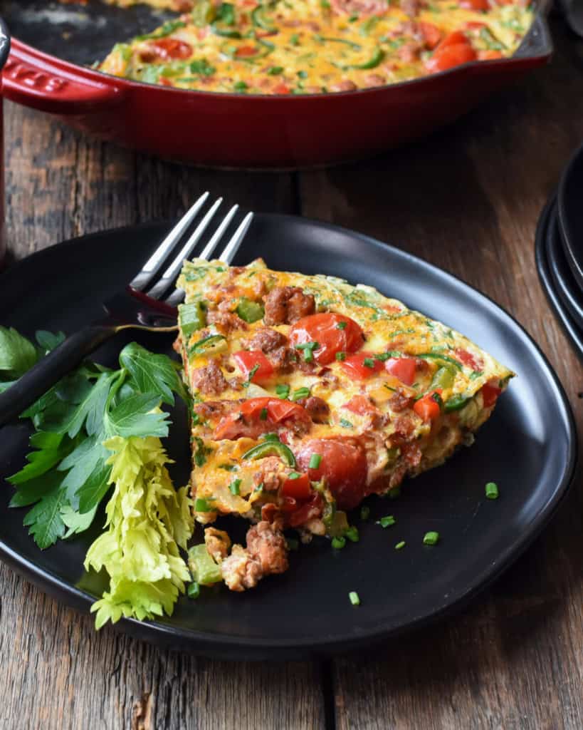 A slice of a hot Italian sausage frittata on a plate with a skillet in the background.