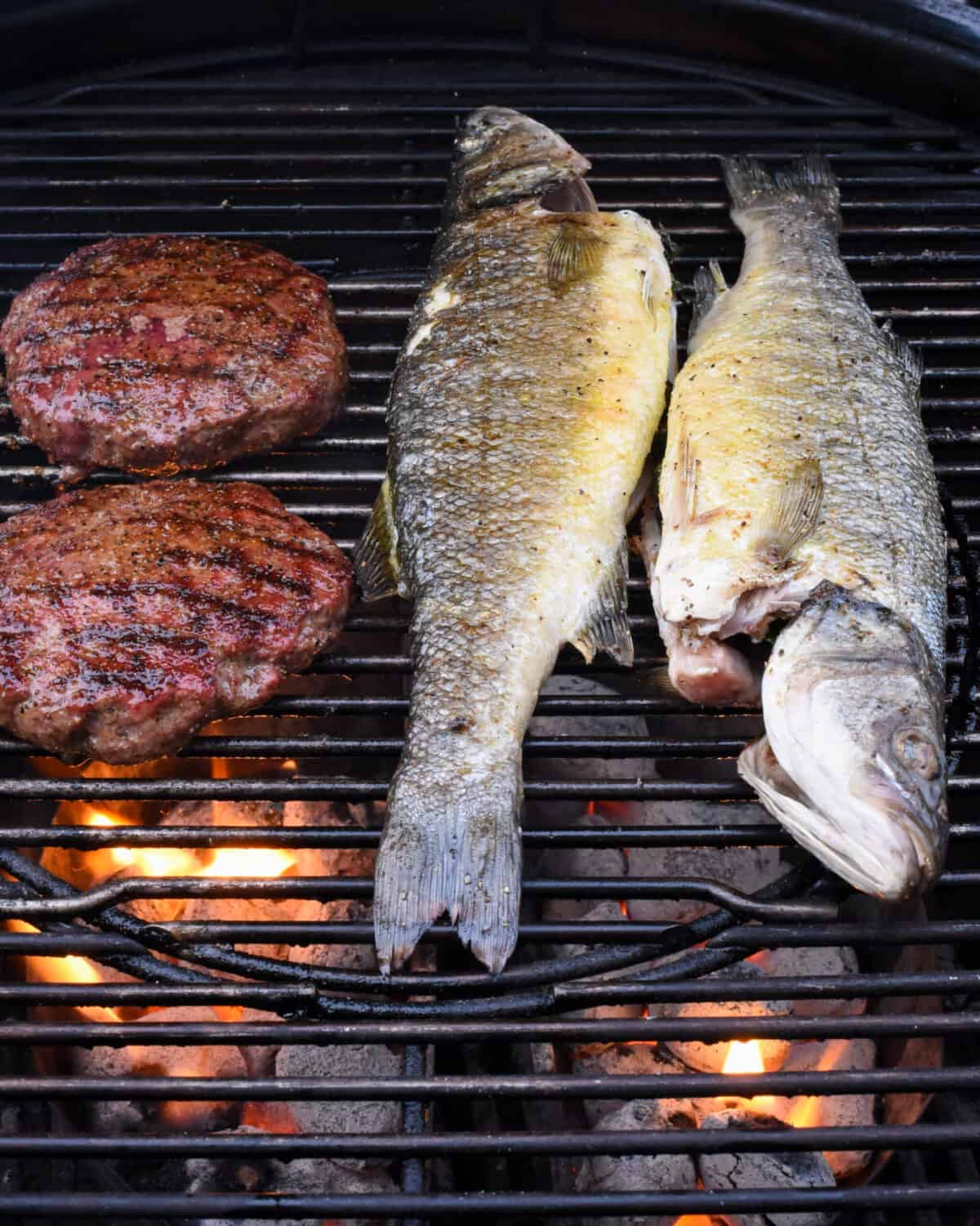 Two whole sea bass and two burgers on the grill.