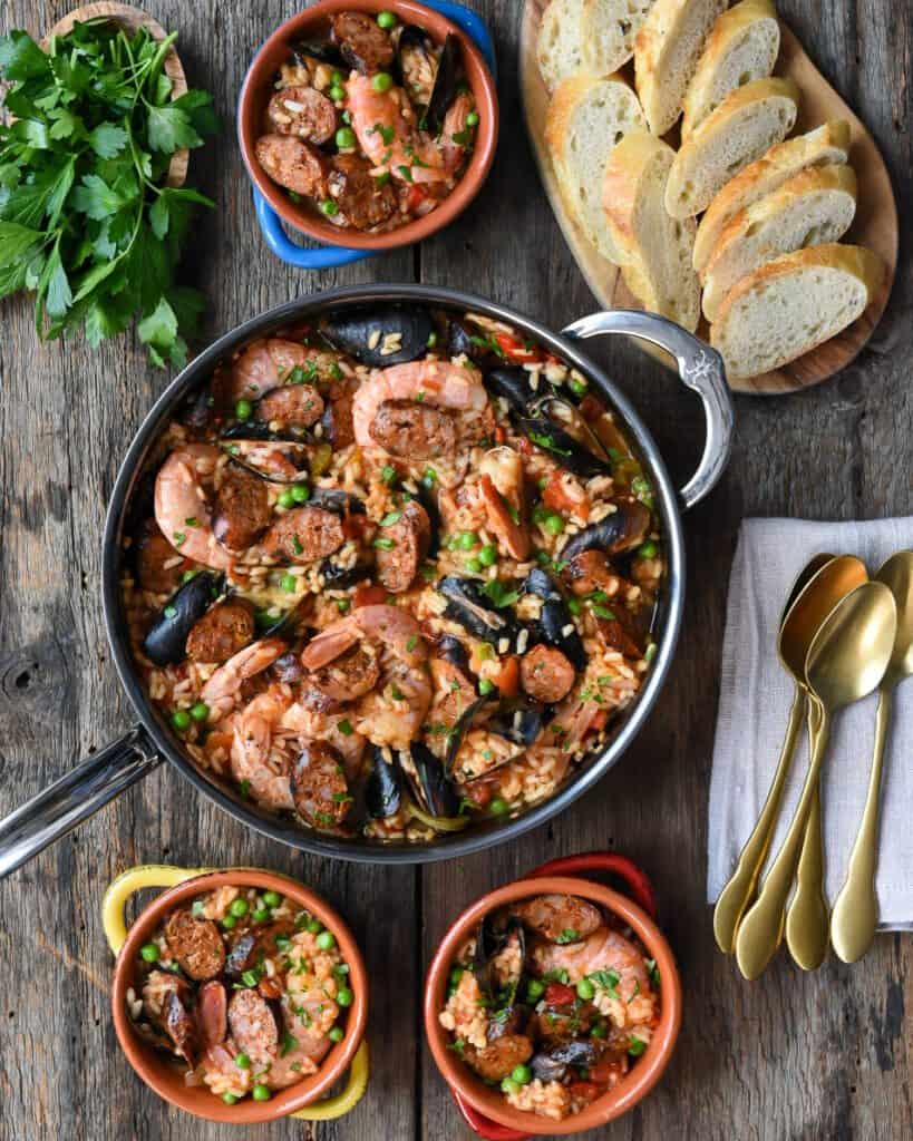 Ontario Pork Hot Italian sausage paella in soup bowls and Hestan NanoBond pan with bread and gold spoons.
