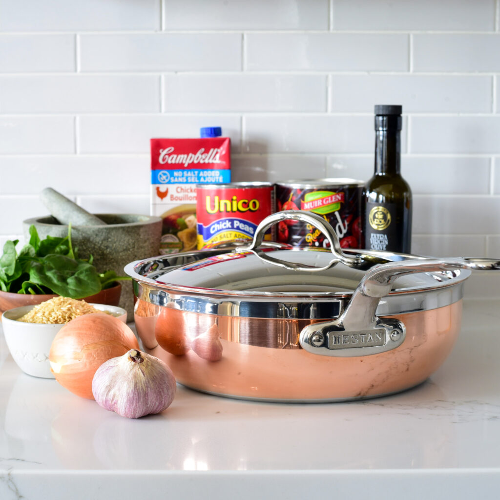 A variety of pantry ingredients and copper pan with lid ready to start cooking.