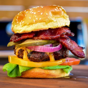 A stacked cheese and bacon burger with pickle and marinated onions.
