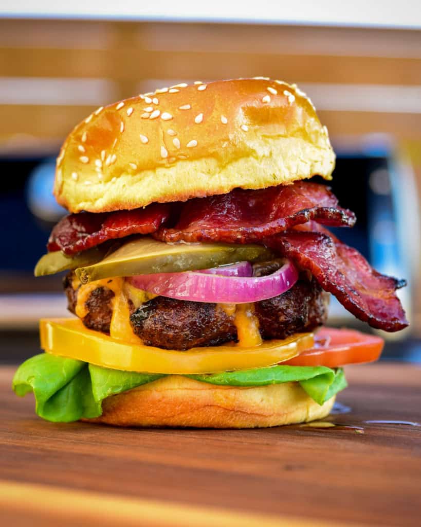 A stacked cheese and bacon burger with pickle and marinated onions.