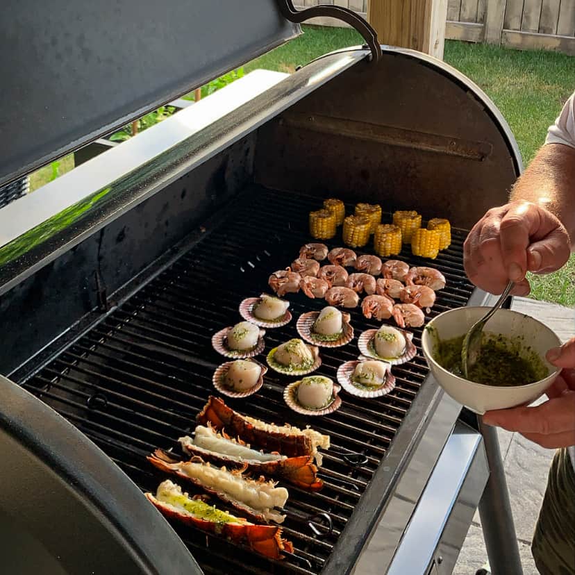 A top down view of a grilled mixed seafood platter with skewered lobster tails, scallops in the shell, skewered shrimp and corn.