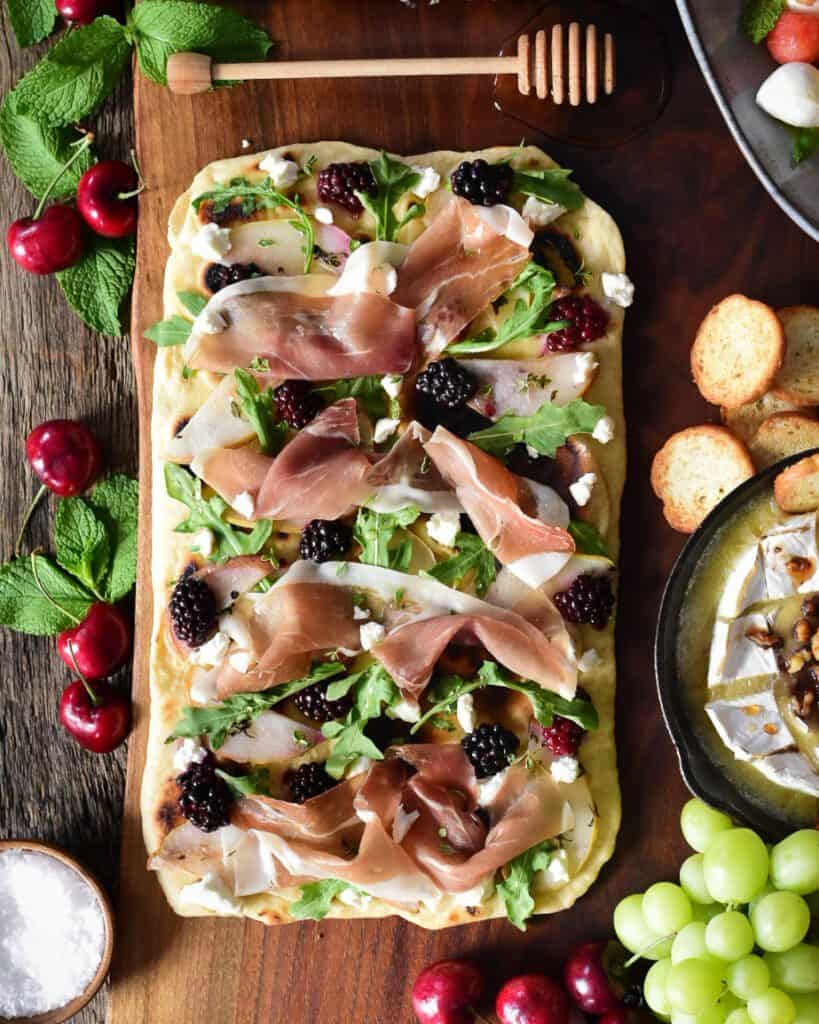 Flatbread with Prosciutto, Poached Pears & Blackberries. Surrounded by honey, brie, grapes and cherries.