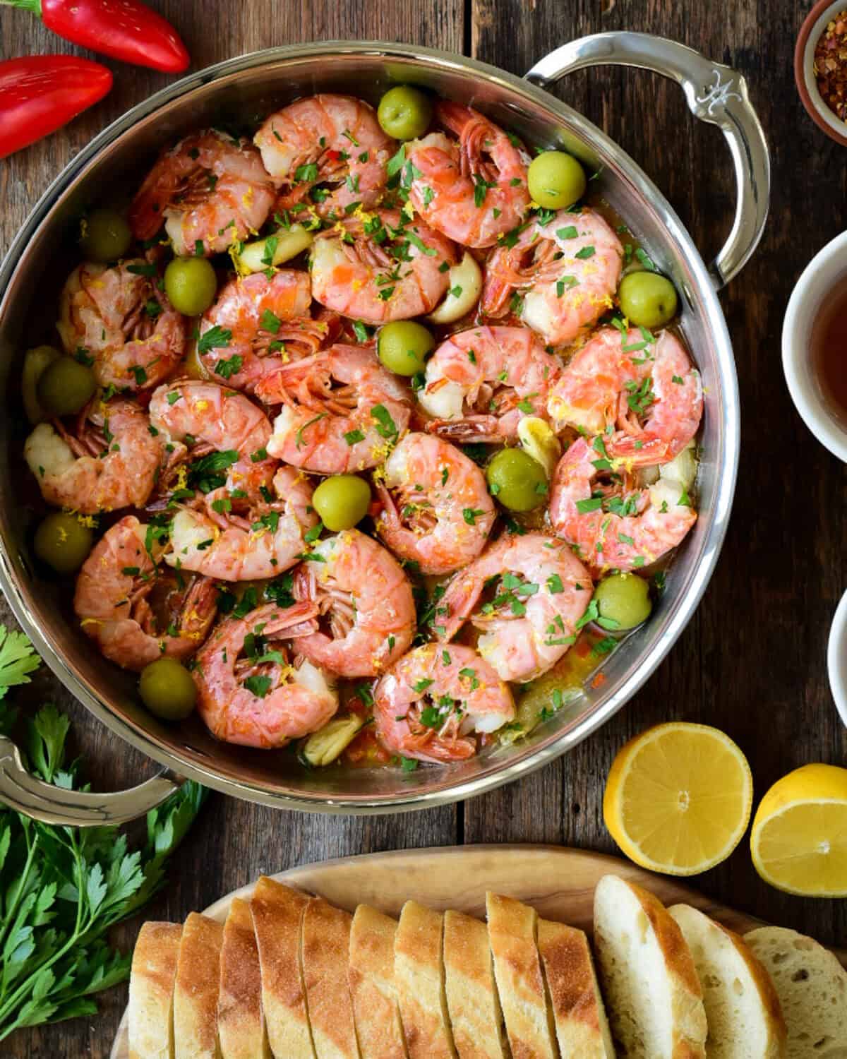 A skillet full of Gambas al Ajillo (garlic shrimp) with slices of bread and lemon.