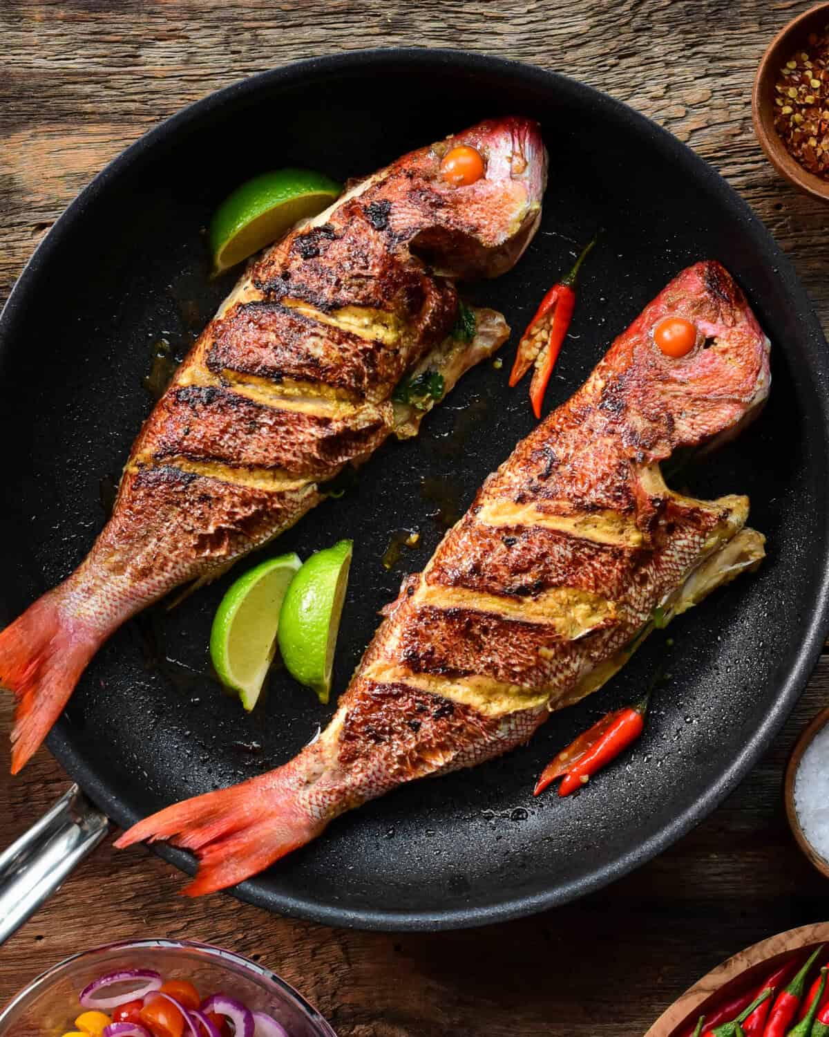 Two pan-fried whole snapper fish in a pan.